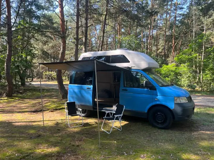Błękitny VW T5 z markizą i krzesłami na kempingu w lesie
