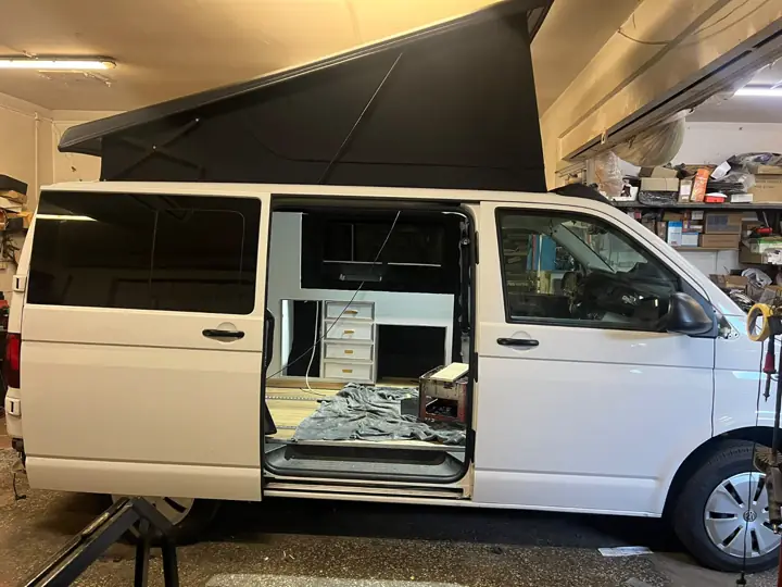 Biały VW T6 z rozłożonym dachem w warsztacie, otwarte drzwi przesuwne